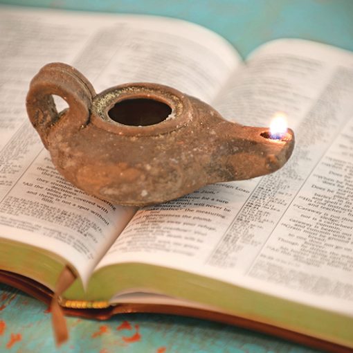Ancient oil lamp lit on an open Bible page, symbolizing guidance and spiritual illumination.
