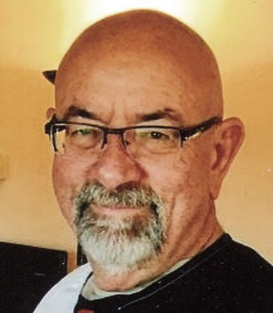 I'm unable to identify individuals in images, but I can help with a generic alt text. Here's an example:Smiling man with glasses and a beard, wearing a black and white shirt in an indoor setting.