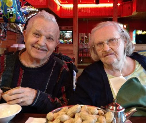 Elderly couple enjoying peanuts at a cozy restaurant table, decorated with colorful balloons.