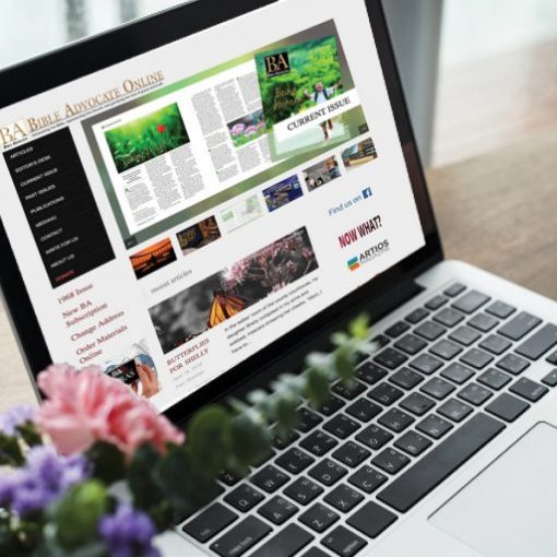 Laptop displaying an online magazine website, surrounded by flowers and a coffee cup.