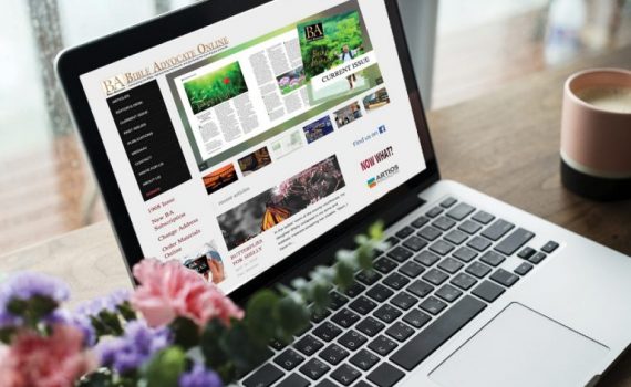 Laptop displaying an online magazine website, surrounded by flowers and a coffee cup.