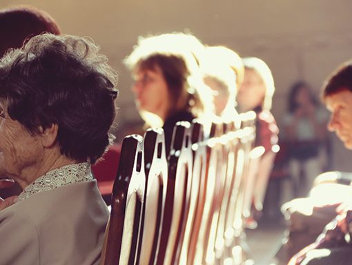People seated in a row of wooden chairs, bathed in warm sunlight during a gathering.