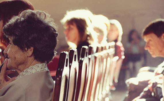 People seated in a row of wooden chairs, bathed in warm sunlight during a gathering.