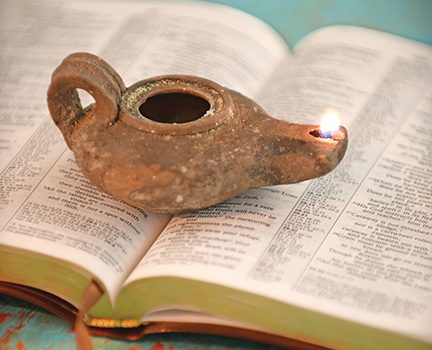 Ancient oil lamp burning on open book pages, symbolizing knowledge and enlightenment on a rustic turquoise surface.