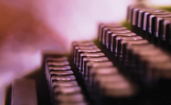 Close-up of blurred vintage typewriter keys, highlighting rows of metallic buttons in soft focus.