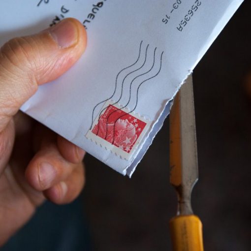 Hand opening a stamped envelope with scissors.