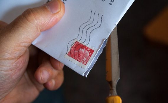 Hand opening a stamped envelope with scissors.