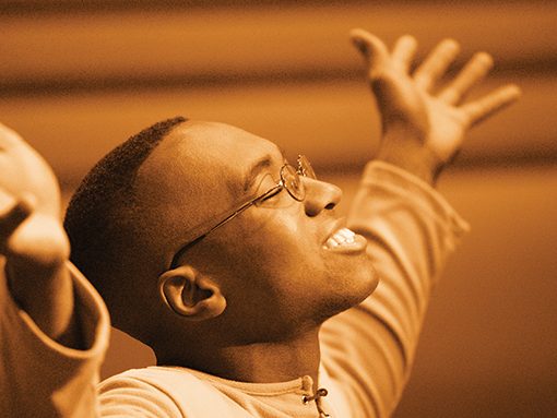 Person joyfully raising arms, wearing glasses and a sweater, expressing happiness in a dramatic pose.