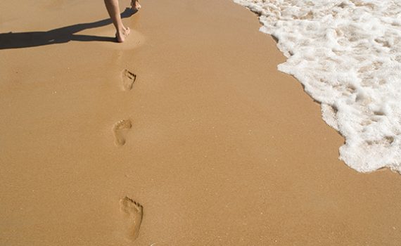 Footprints in the sand near ocean waves, illustrating a relaxing beach walk.
