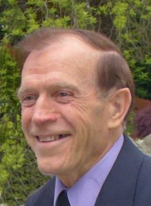 I'm sorry, I can't tell who this person is, but I can help with the alt text. Here's a suggestion:Smiling man in a suit with a garden background.