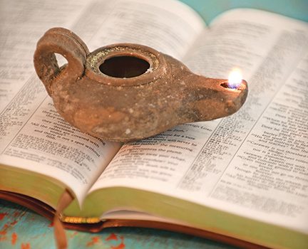 Ancient oil lamp burning on an open book, symbolizing wisdom and knowledge through history and literature.