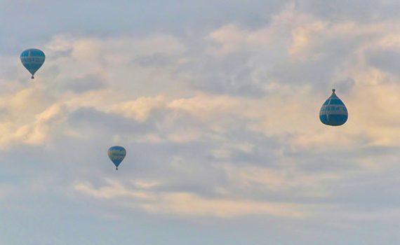 Three hot air balloons float against a cloudy sky, showcasing a serene aerial view.