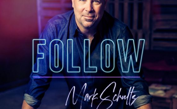 A person in a denim shirt with text FOLLOW overlayed in a dimly lit room, creative ambiance.