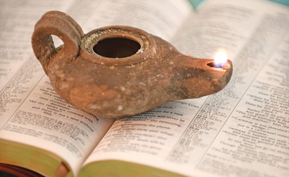 Ancient oil lamp lit atop an open Bible, symbolizing light and wisdom in spirituality and history.