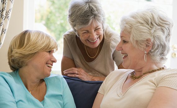 Elderly women laughing and chatting together in a cozy living room setting, showcasing friendship and joy.