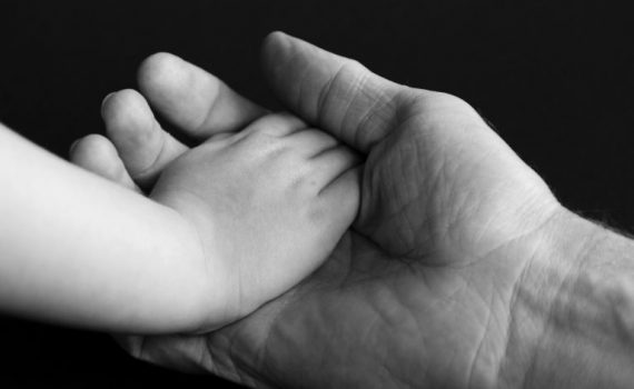 Adult hand holding a child's hand, symbolizing care and support. Black and white close-up image.
