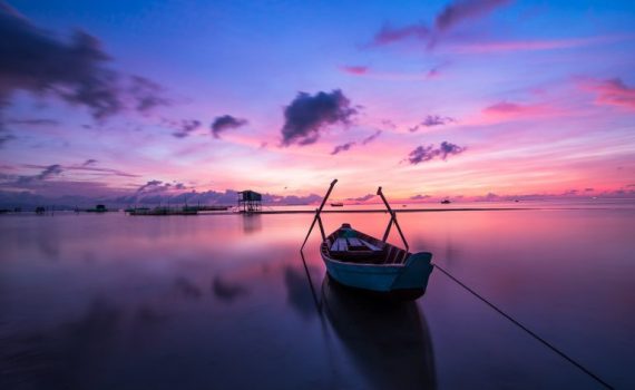 Boat on tranquil water at sunrise with vibrant pink and blue sky, reflecting serene scenery and peaceful atmosphere.