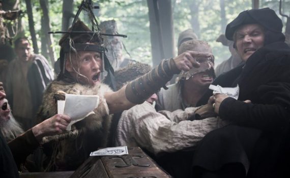 People in medieval costumes engaged in an intense dispute in a forest setting.