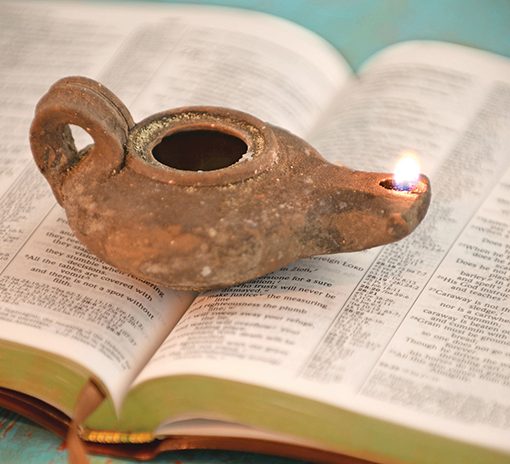 Ancient oil lamp lit atop open book, symbolizing illumination and knowledge.