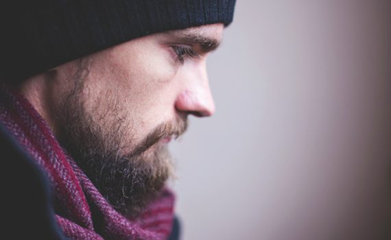 Man in a black beanie and maroon scarf, side profile with a contemplative expression.
