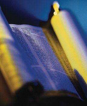 Open scroll with text in low light, reflecting a mix of blue and yellow hues, conveying a sense of historical depth.