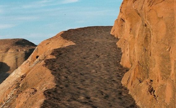 Narrow dirt path along a rocky cliff with clear blue sky in the background.