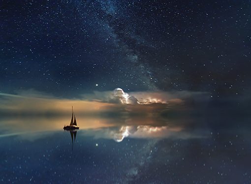 Sailboat under starry night sky and Milky Way reflection on calm water. Dreamy tranquil scene.