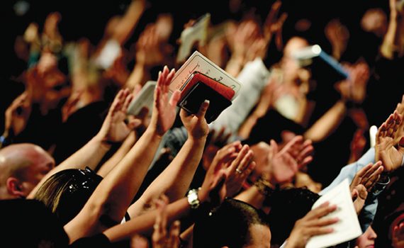 A crowd of people raising hands, holding books, in a vibrant gathering or event.