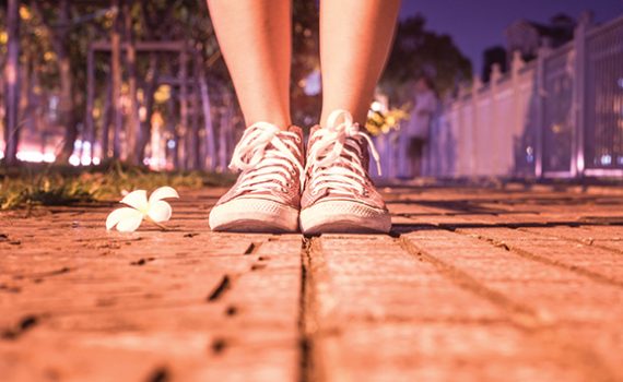 Sneakers on sidewalk next to flower in evening light, signifying a peaceful urban stroll.