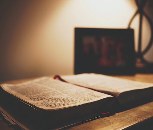 Open book on a wooden table under soft lighting, with a blurred photo frame in the background, creating a serene ambiance.