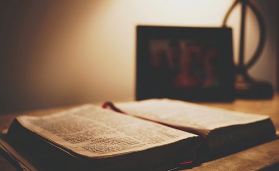 Open book on a wooden table under soft lighting, with a blurred photo frame in the background, creating a serene ambiance.