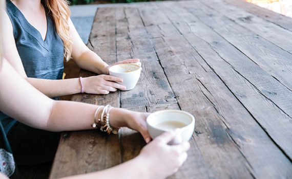 Two people enjoying coffee at a rustic wooden table outdoors.
