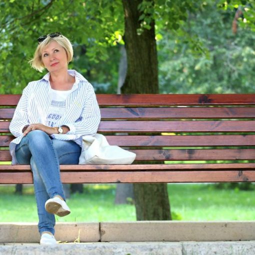 Woman relaxing on a park bench, wearing casual attire, surrounded by lush greenery.