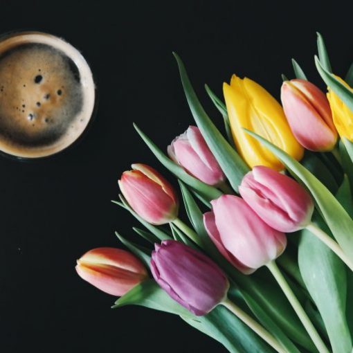 Colorful tulips next to a coffee cup on a dark background, creating a vibrant, cozy atmosphere.