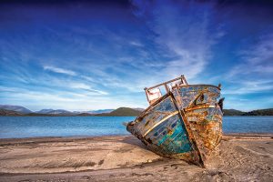 Old, weathered boat on a sandy shore under a blue sky, highlighting coastal landscapes and serene seascapes.