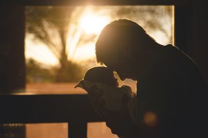 Silhouette of a parent holding a baby at sunset by a window, symbolizing love and bonding.