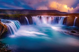 Spectacular waterfall at sunrise with vibrant sky and misty water, creating a serene and mystical natural landscape.