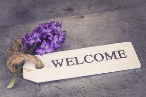 Welcome sign with purple flowers on rustic background, conveying hospitality and warmth.