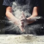 Person clapping hands with flour in kitchen, creating a cloud-like effect. Perfect for baking or cooking theme.