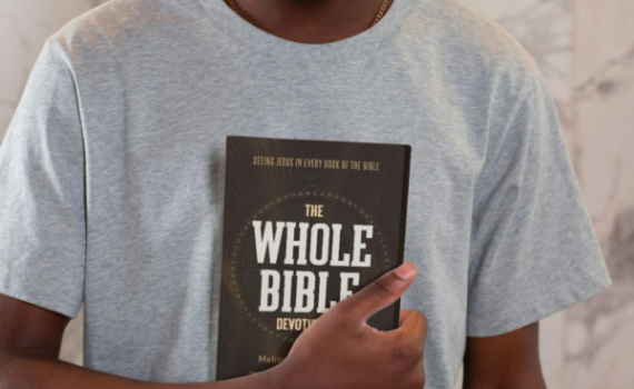 Person holding a book titled The Whole Bible Devotional against a marble background.