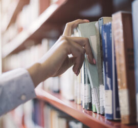 Hand selecting a book from a library shelf, emphasizing reading and education.